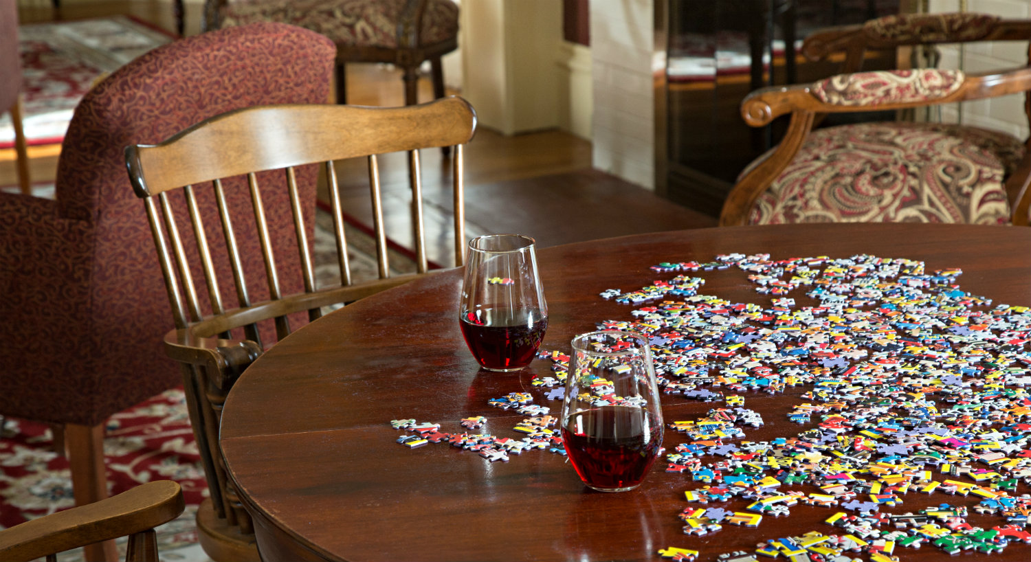 A puzzle is laid out on a wooden table with two stemless wine glasses.