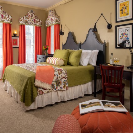 A king sized bed covered in green bedding accented with orange in a room with green walls and beige carpet.