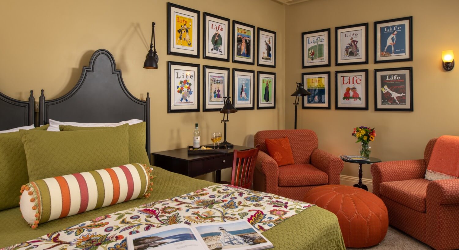 Bedroom with gold walls and a large ornate antique wooden bed made up in green and floral bedding with a seating area.