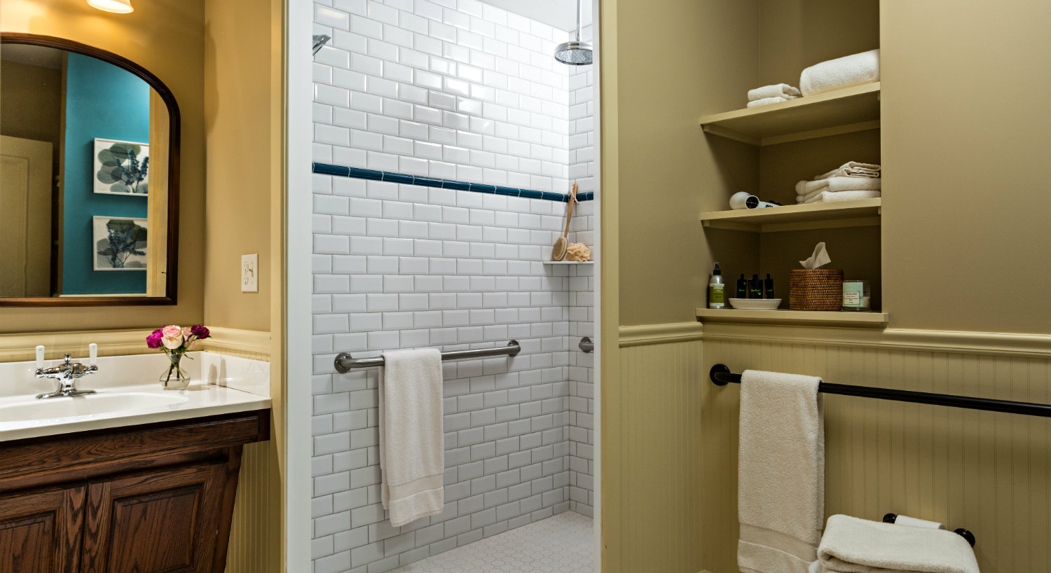 Bathroom with while tiled shower and a wooden vanity with a mirror and built-in storage.