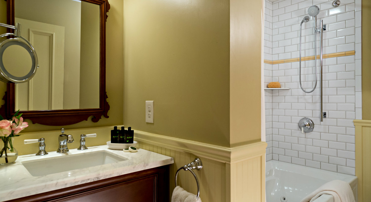 Bathroom with cream chair rail and beige walls, wooden vanity and white tiled tub-shower combo.