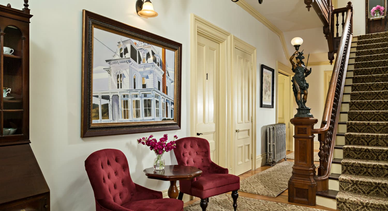 Foyer area with two ruby velvet chairs and a tall staircase rising to the second floor.