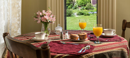A table with a striped cloth set for breakfast with muffins, coffee and juice.