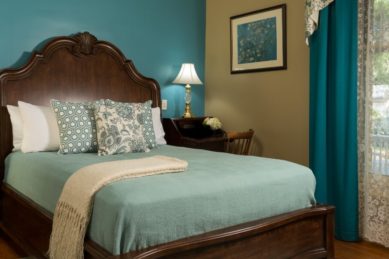 Large wooden bedframe with bed made up in green with decorative pillows in a room with teal walls.