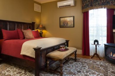 Guest room with tan walls and a large wooden bedstead and a standalone fireplace.