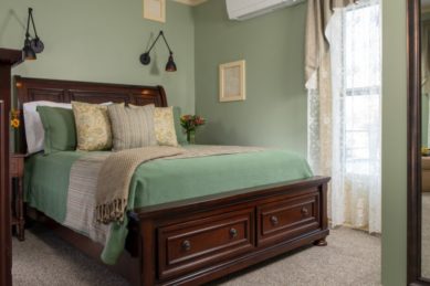 Large wooden bedframe with bed made up in green with decorative pillows in a room with teal walls.