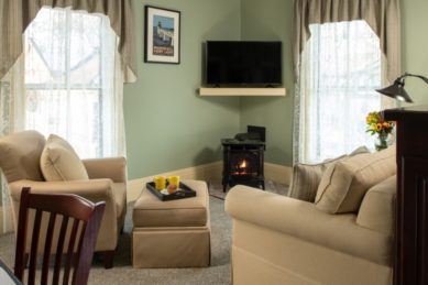 A seating arrangement with beige chairs next to a tv on the wall and a small working fireplace.