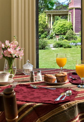 A table with a striped cloth set for breakfast with muffins, coffee and juice.