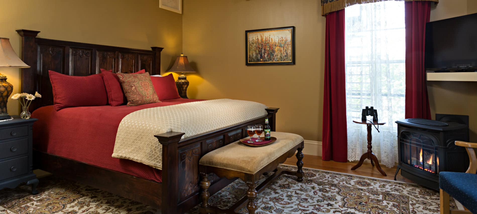 Guest room with tan walls and a large wooden bedstead and a standalone fireplace. 