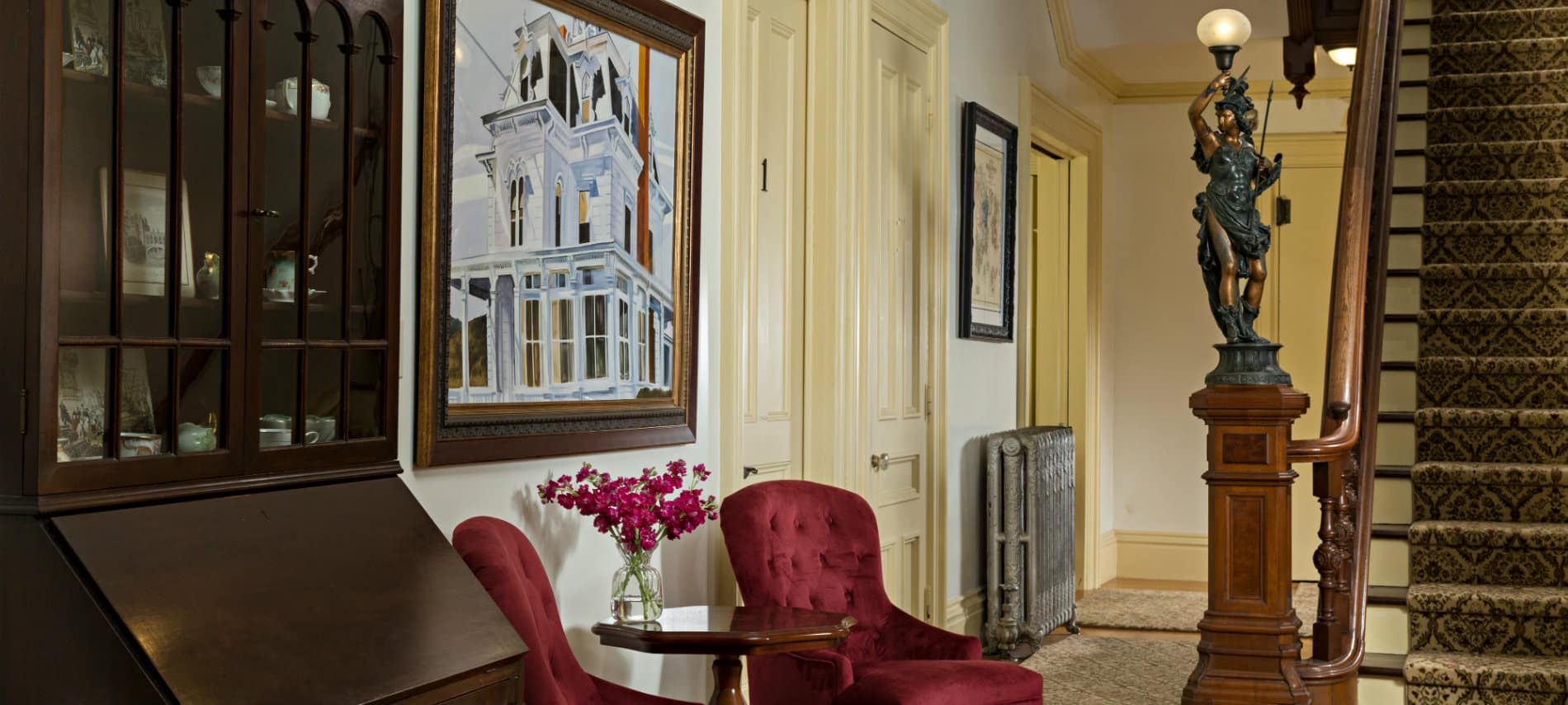 Foyer area with two ruby velvet chairs and a tall staircase rising to the second floor.